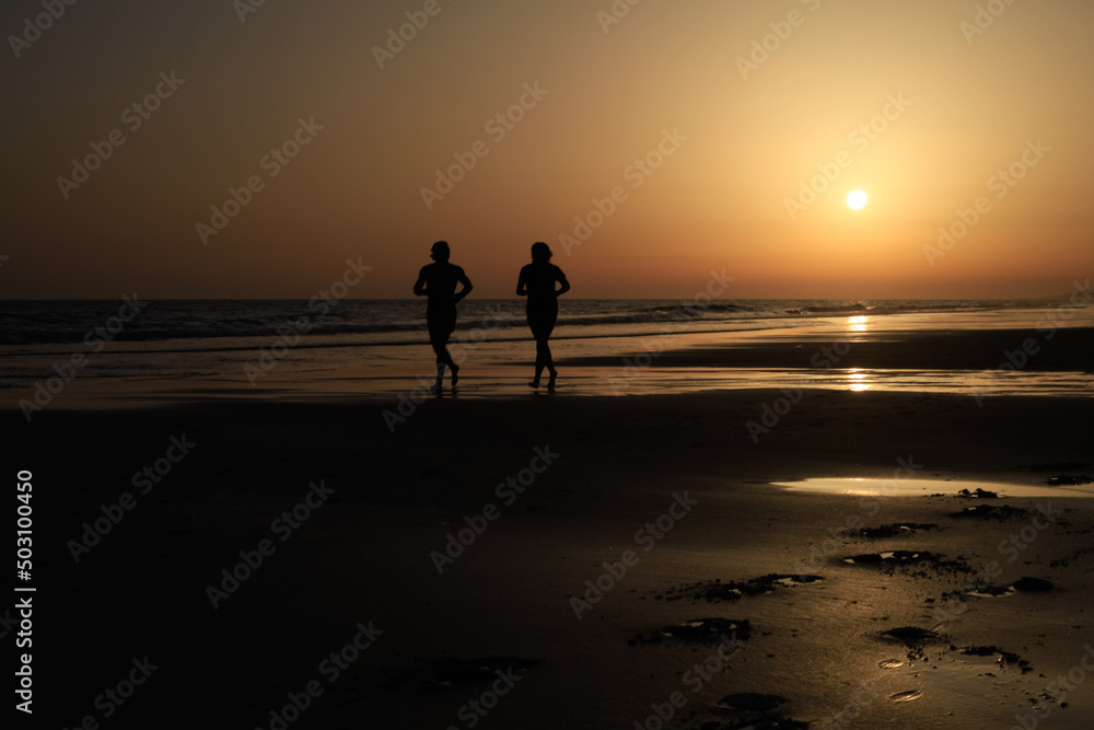 long shot of two runners on a great spanish beach at sunset