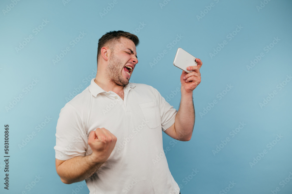 Portrait of a joyful man with a smartphone in his hand on a blue background emotionally rejoices and shouts Portrait of a joyful man with a smartphone in his hand on a blue background emotionally rejoices and shouts