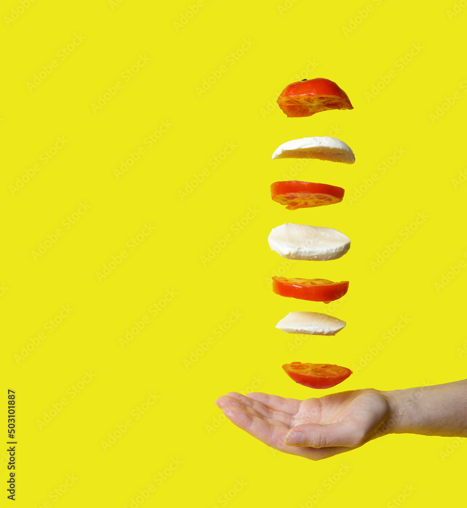 flying tomato and mozzarella isolated on yellow background. frozen motion. mozzarella and tomato soar over hand. copy space flying tomato and mozzarella isolated on yellow background. frozen motion. mozzarella and tomato soar over hand. copy space