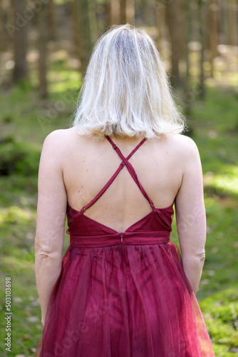 Woman wearing backless magenta gown standing in forest. photo