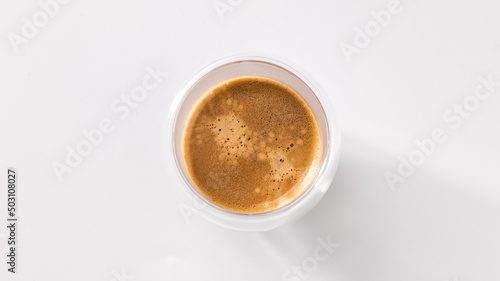 Freshly brewed coffee in a glass cup on a white background, top view, central composition © mira_y