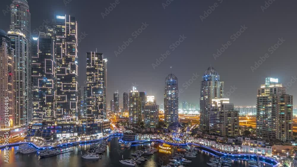 Dubai marina tallest skyscrapers and yachts in harbor aerial night panoramic timelapse. View at apartment buildings, hotels and office blocks, modern residential development of UAE
