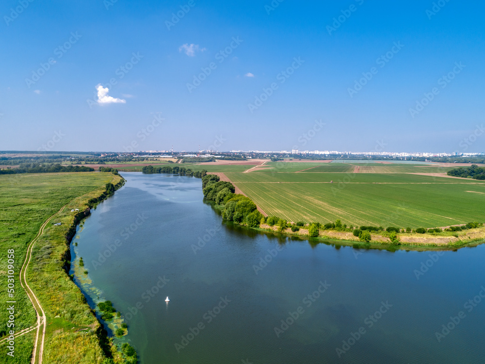 Large green field and trees near tranquil river in spring