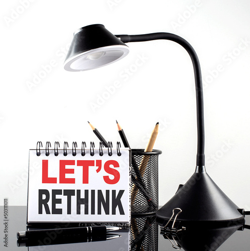 LET S RETHINK text on notebook with pen and table lamp on the black background photo