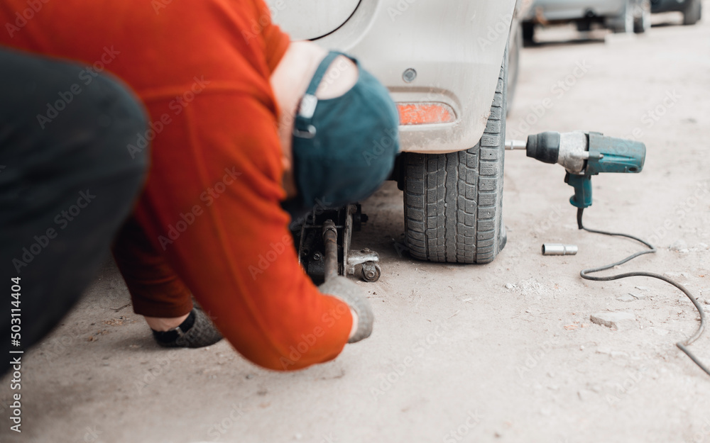 Repair broken car concept. Rear view of mechanic jacking up vehicle outdoors, close-up. Selective focus on wheel Repair broken car concept. Rear view of mechanic jacking up vehicle outdoors, close-up. Selective focus on wheel