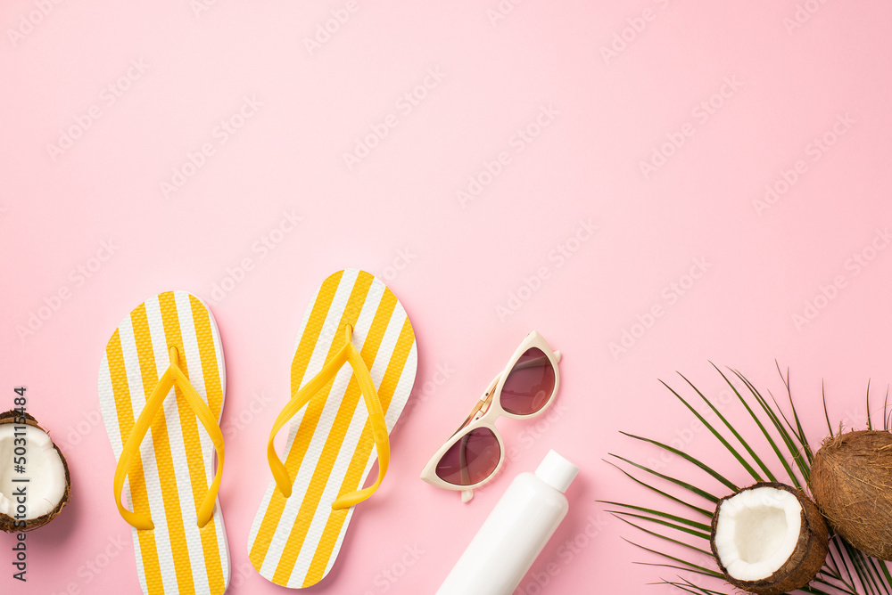 Summer holidays concept. Top view photo of sunglasses striped yellow slippers sunscreen tube cracked coconuts and palm leaves on isolated pastel pink background with copyspace
