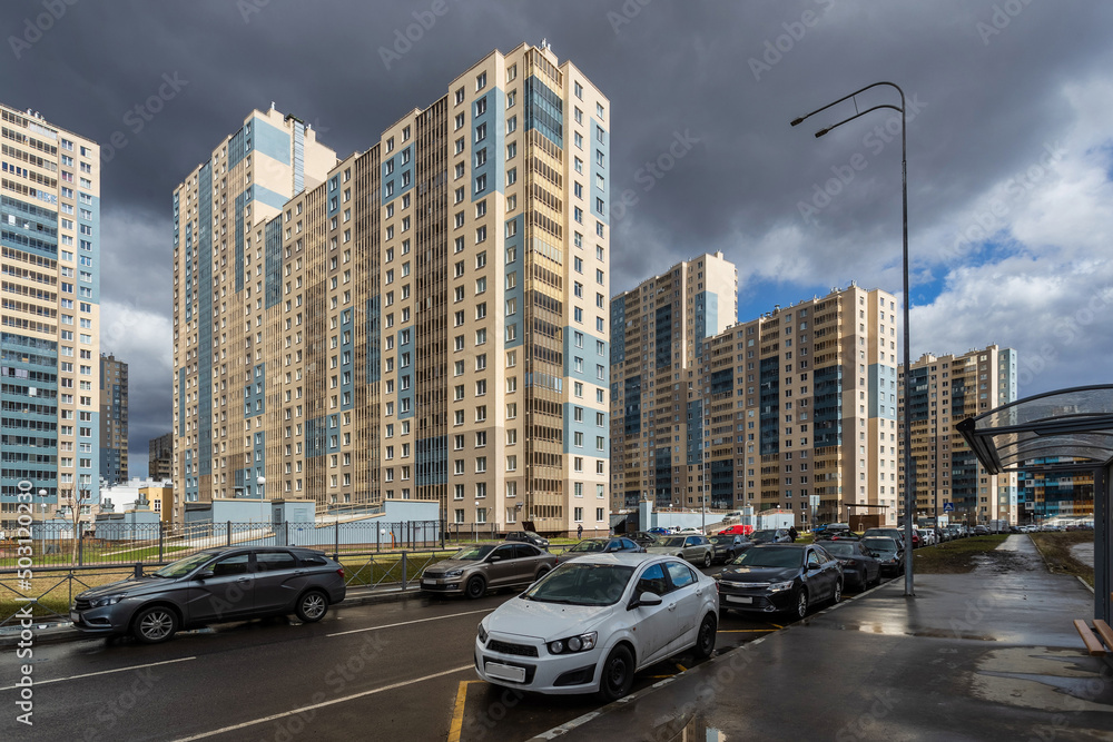 Fototapeta premium Multi-apartment residential buildings along the street, illuminated by the bright sun facades, against the background of a sky with dark clouds.