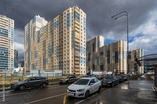 Multi-apartment residential buildings along the street, illuminated by the bright sun facades, against the background of a sky with dark clouds. © SFotoz