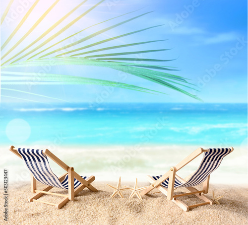 Vacation holidays background concept - two beach lounge chairs under palm on summer beach.