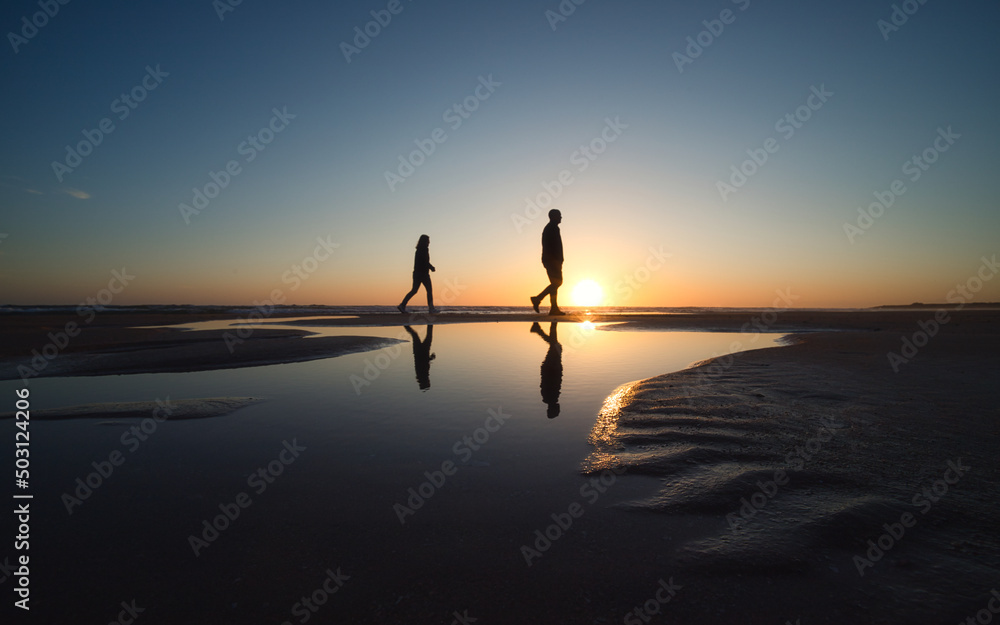 Silhouette von zwei Personen die während des Sonnenuntergangs am Strand spazieren gehen