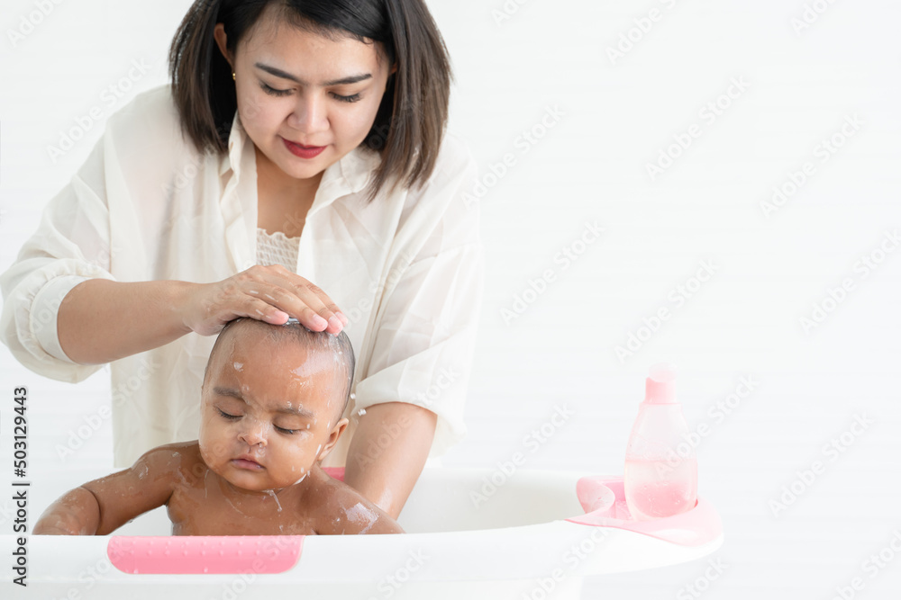 Cute African newborn baby bathing in bathtub with soap bubbles on head and body. Asian young