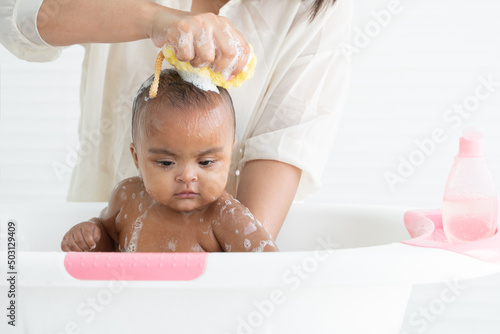 Slika na platnu Cute African newborn baby bathing in bathtub with soap bubbles on head and body