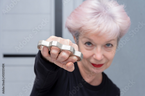 фотографія An elderly woman strikes with brass knuckles on a light background, close-up, selective focus