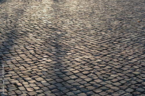 Fototapeta Empty old uneven cobblestone street pavement under sunlight