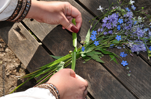 Rapariga a fazer um pequeno ramo de flores campestres naturais, a amarrar os pés das flores com um erva para segurar, tudo pousado numa superfície de traves de madeira photo