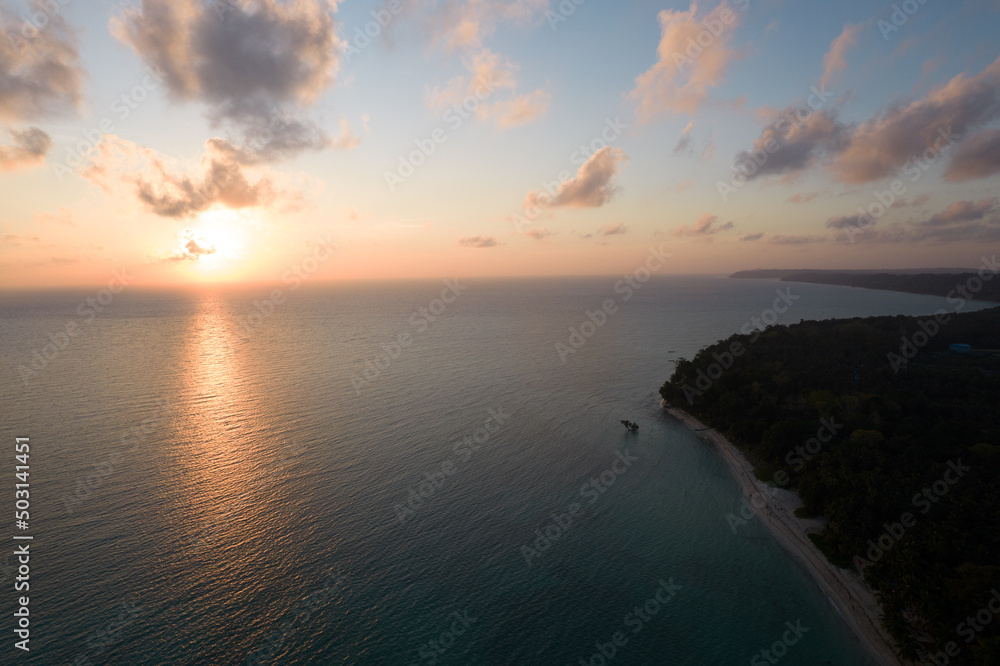 aerial drone shot going from red orange sunrise on horizon to green coconut tree covered island at dawn dusk at swaraj dweep havelock langkawi islands in India Asia