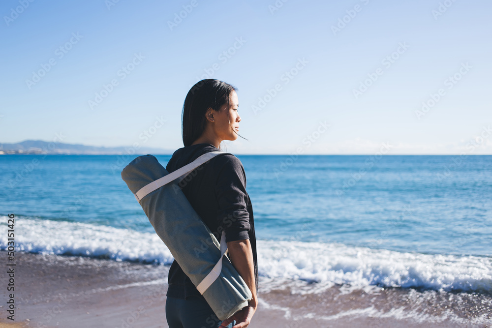 Young female trainer in sportswear looking at sea horizon while choosing place for coastline workout on weekend,attractive Asian woman with bag mat thinking about healthy lifestyle and body positive Young female trainer in sportswear looking at sea horizon while choosing place for coastline workout on weekend,attractive Asian woman with bag mat thinking about healthy lifestyle and body positive