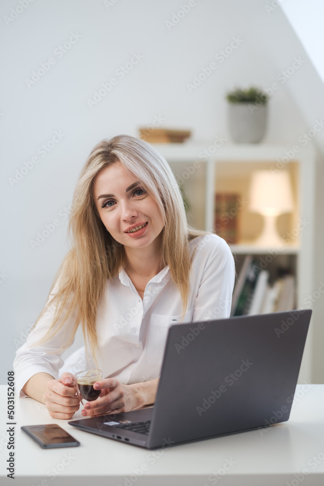 Young beautiful caucasian blonde woman working on laptop at home and drinking coffee. Remote work or freelance. Young beautiful caucasian blonde woman working on laptop at home and drinking coffee. Remote work or freelance.