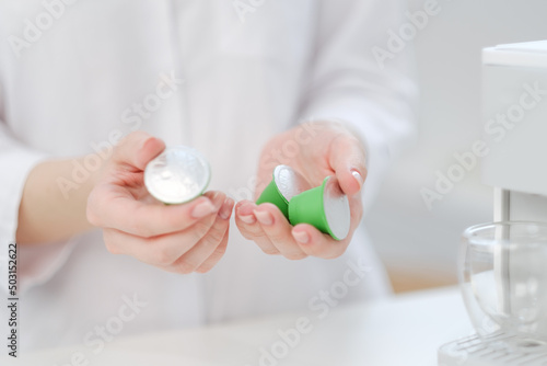 A woman holds coffee capulas in her hands and prepares espresso in a capsule coffee machine. White background. A bright room.