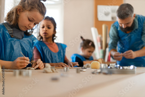 Group of little kids with teacher working with pottery clay during creative art and craft class at school.