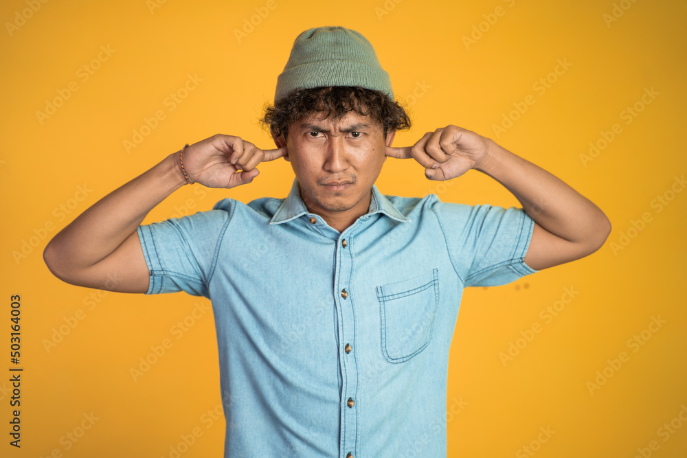 Stressed asian young man cover his ear does not want to hear anything over isolated background