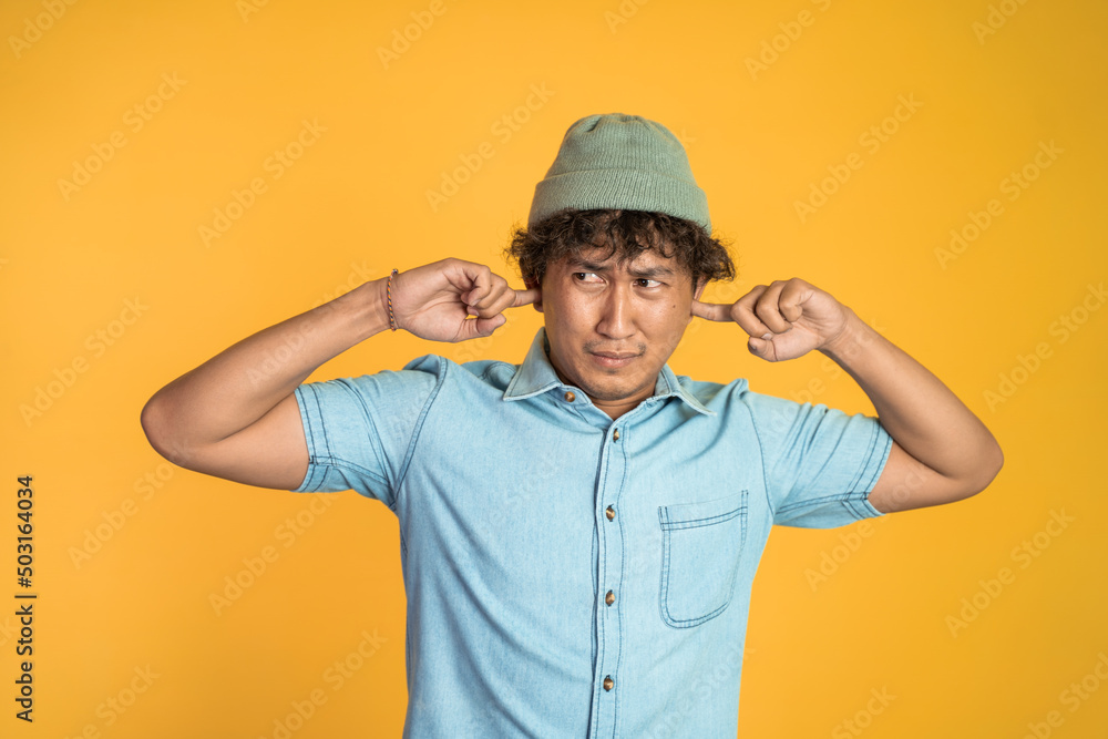 Stressed asian young man cover his ear does not want to hear anything over isolated background