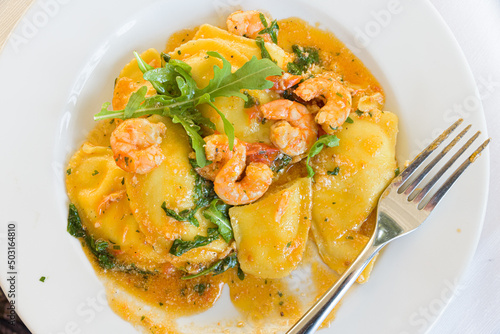 Acciaroli, Italy. Plate of pumpkin stuffed ravioli, with shrimp, in a plate with fork on a restaurant table.
