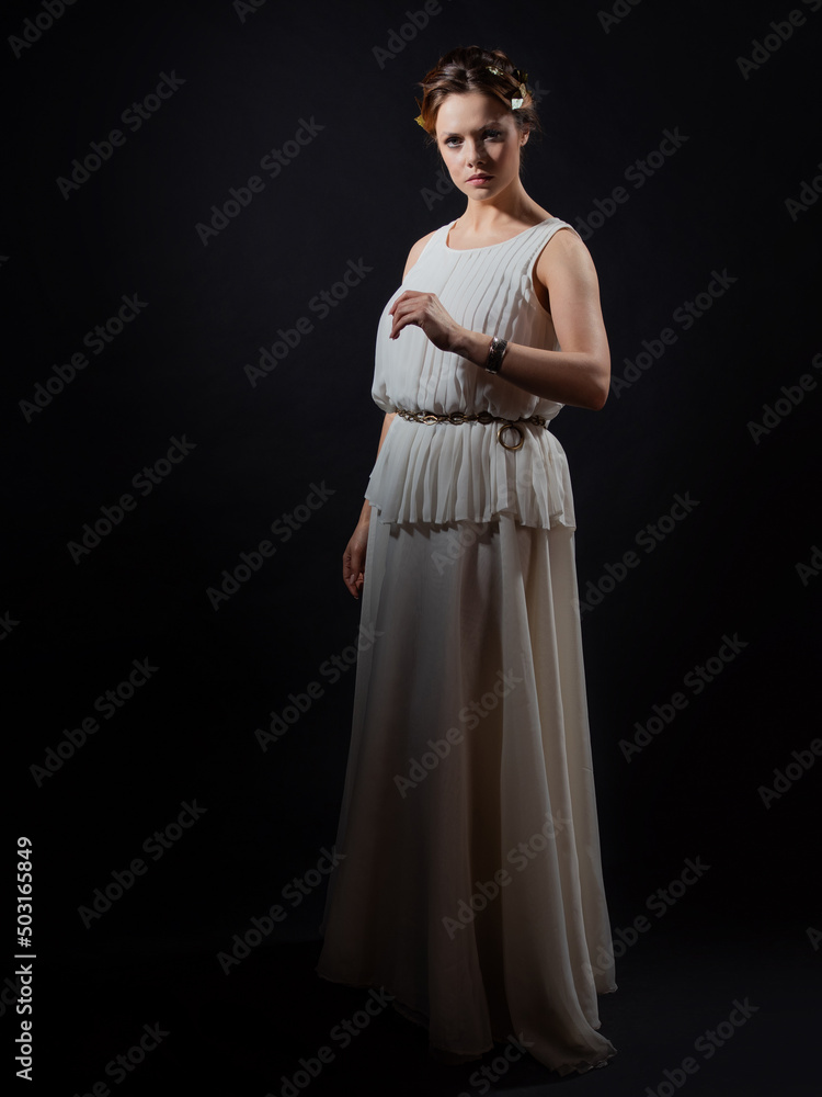 An ancient heroine, a young woman in the image of an ancient Greek goddess or muse. A noble heroine in a white tunic and a laurel wreath, a full-length photo on a black background An ancient heroine, a young woman in the image of an ancient Greek goddess or muse. A noble heroine in a white tunic and a laurel wreath, a full-length photo on a black background