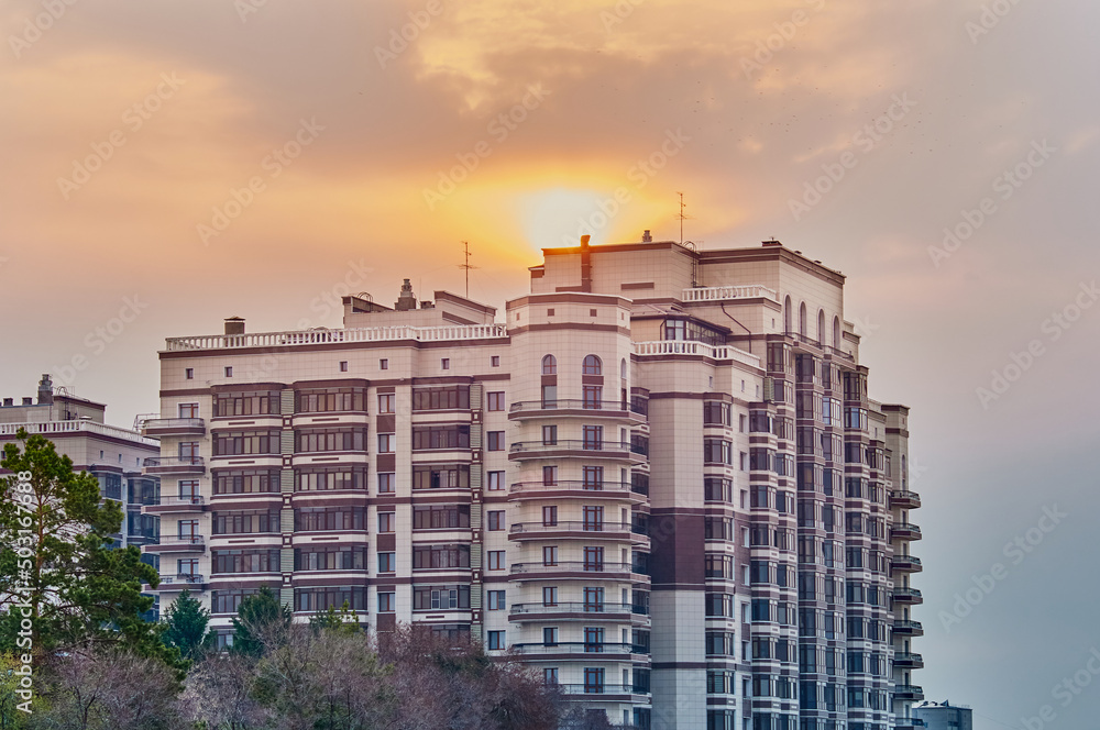 Fototapeta premium Above the roof of an apartment building, the sun peeks out from behind the clouds. Summer morning.