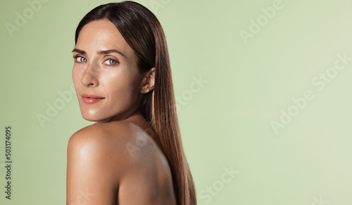 Beautiful female model, 40s years old, has perfect shiny, glowing body, facial skin, nourished and hydrated face after spa, cosmetic procedure, green background