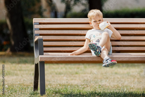 Cute little boy sitting on a bench and drinks juice.