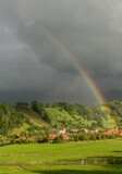 Stormy sky with a rainbow over a green hill with houses. Countryside