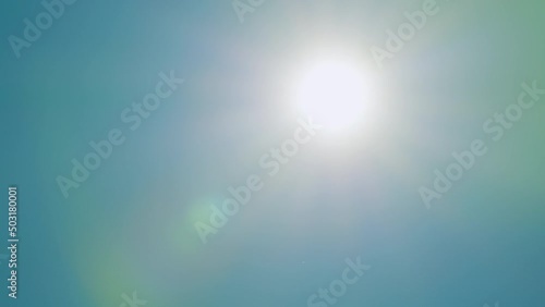 Beautiful sparkle sun moves across clear blue sky. Sun rays light isolated on blue background. Real time.