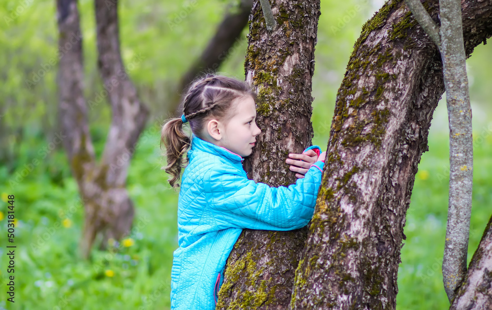 A girl hugs a tree in the spring garden. A child expressing a love of nature. A girl hugs a tree in the spring garden. A child expressing a love of nature.