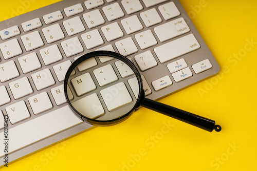 Magnifying glass on a keyboard on a yellow background. Internet search concept