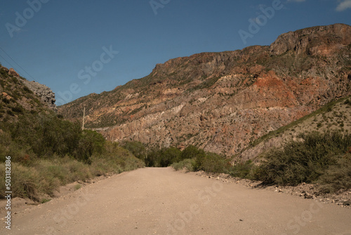 Traveling into the desert. View of the dirt road across the arid environment, rock and sandstone mountains. © Gonzalo