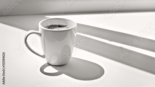 Obraz na płótnie White cup of coffee on a sunlit window sill black and white w salonie