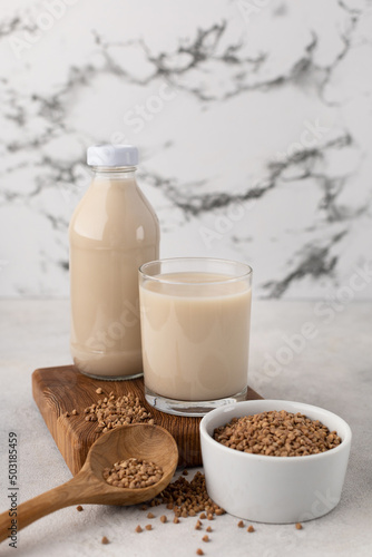 Bottle of vegetable milk from buckwheat with an ingredient in a bowl on a light background