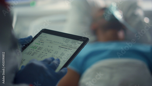 Doctor holding tablet screen checking patient medical history in ward closeup.