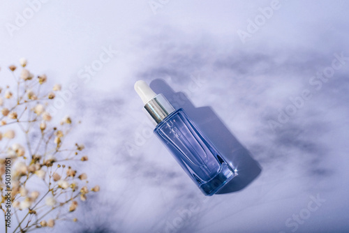 Purple serum bottle and gypsophilla flowers, hard shadows. Natural cosmetics, spa and wellness concept. Top view