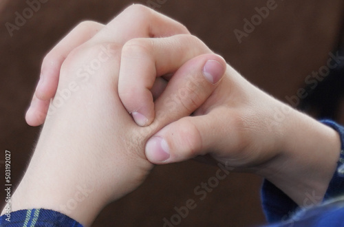 The teenager sits and clasps his hands. Close-up of hands.