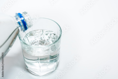 Pouring pure fresh mineral non-carbonated water into a glass beaker on a white background from a plastic bottle.