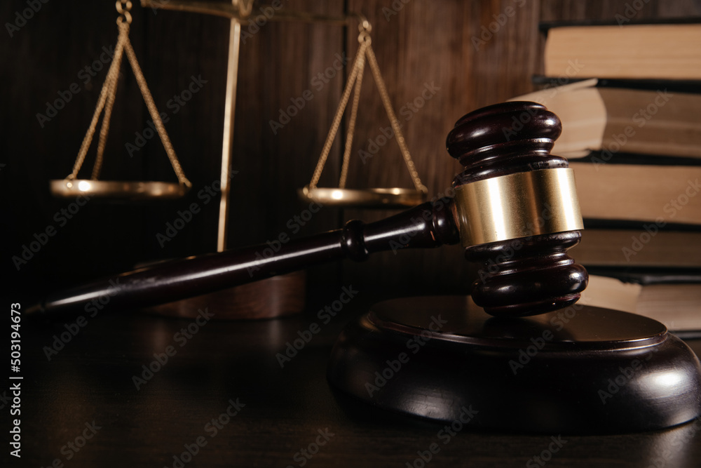 Wooden gavel and scales in a dark court room at wooden desk Wooden gavel and scales in a dark court room at wooden desk