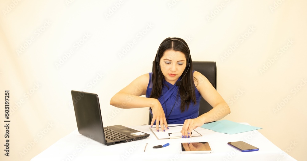 Cute and successful CEO responsible, wearing blue blouse, working hard with her laptop and headset, on a white background Cute and successful CEO responsible, wearing blue blouse, working hard with her laptop and headset, on a white background