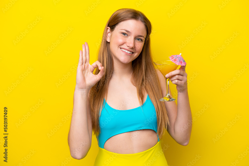 Young caucasian woman holding a cocktail isolated on yellow background showing ok sign with fingers Young caucasian woman holding a cocktail isolated on yellow background showing ok sign with fingers