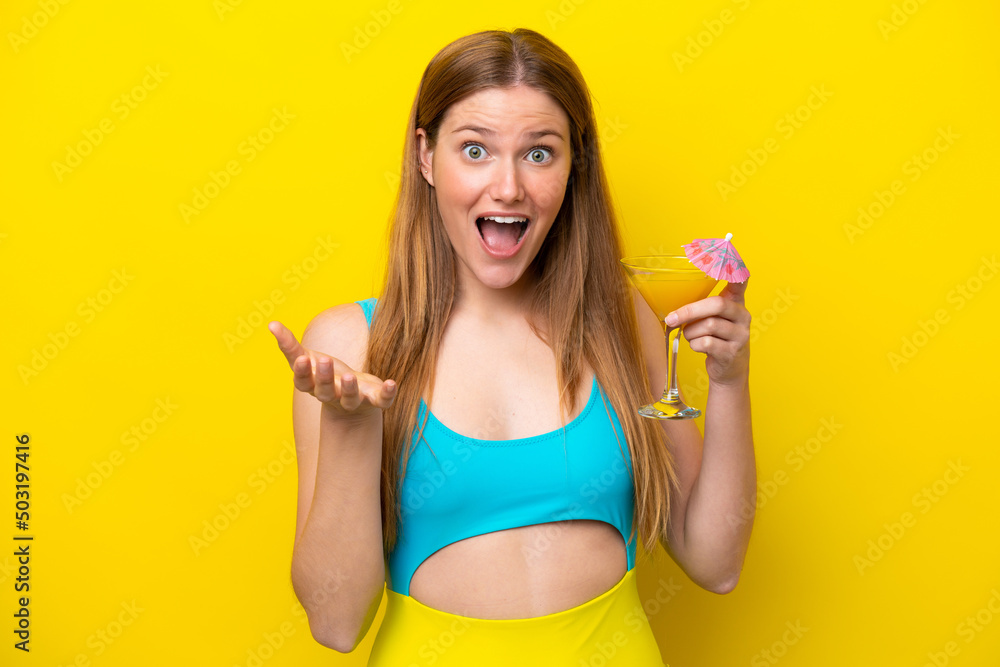 Young caucasian woman holding a cocktail isolated on yellow background with shocked facial expression Young caucasian woman holding a cocktail isolated on yellow background with shocked facial expression