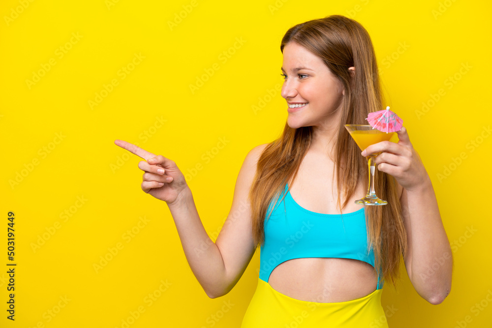 Young caucasian woman holding a cocktail isolated on yellow background pointing to the side to present a product Young caucasian woman holding a cocktail isolated on yellow background pointing to the side to present a product
