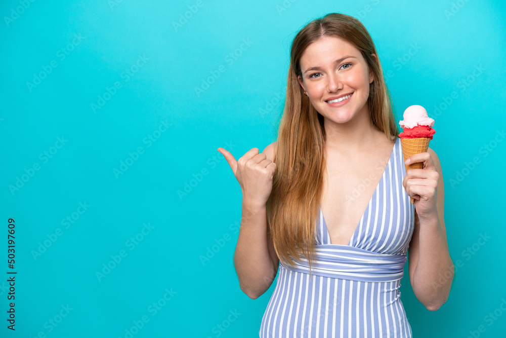 Young caucasian woman in swimsuit eating ice cream isolated on blue background pointing to the side to present a product Young caucasian woman in swimsuit eating ice cream isolated on blue background pointing to the side to present a product