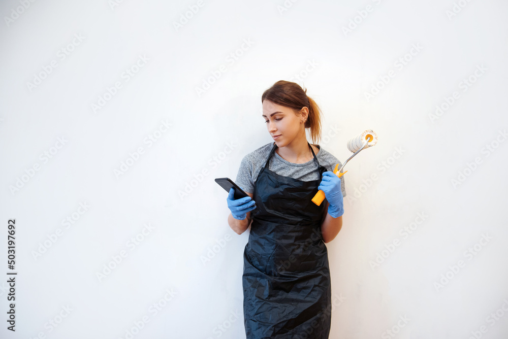 Smiling woman using smartphone, watching tutorials how to paint walls with a roller Smiling woman using smartphone, watching tutorials how to paint walls with a roller
