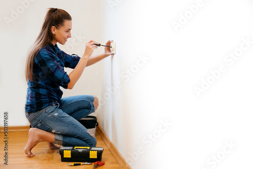 Brunette woman in plaid shirt repairs an electric socket with a screwdriver photo